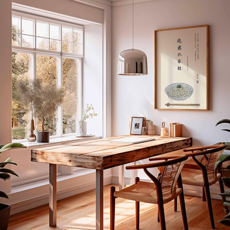 May include: A dining room scene featuring a wooden table with metal legs and two woven chairs. A framed artwork of noodles with chopsticks hangs on the wall. A large window offers a view of trees.