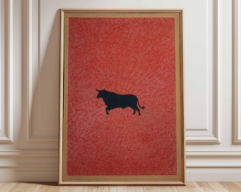 May include: Framed artwork featuring a black silhouette of a bull against a textured red background. The artwork is encased in a wooden frame and displayed on a wooden floor. The red background has a pattern of fine lines.
