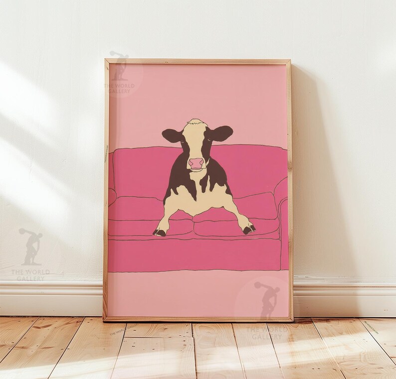 May include: A framed art print showing a cow relaxing on a pink sofa. The cow is illustrated in black and white, with a cream-coloured body. The background is a gradient of pink shades, creating a whimsical and modern aesthetic.
