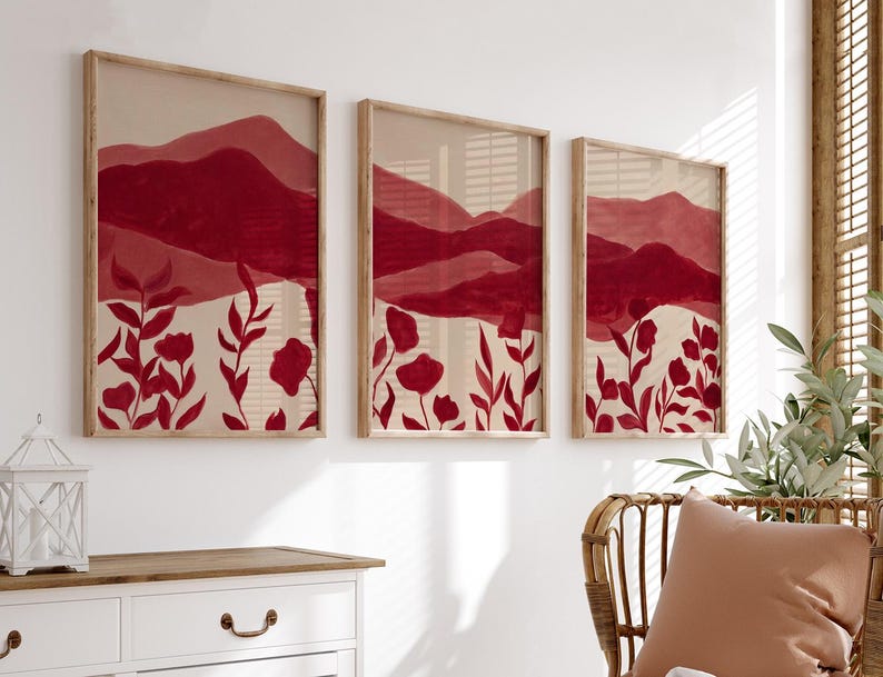 May include: Three framed art prints featuring a watercolor landscape with red mountains and floral elements. The artwork has a neutral background with red flowers and foliage. The frames are made of light-colored wood, creating a cohesive wall art set.