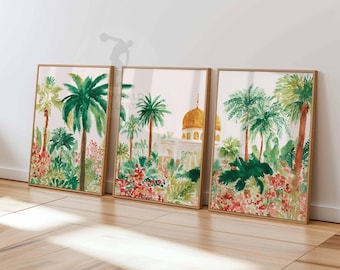 May include: Set of three framed watercolor prints depicting a tropical landscape. The artwork features lush green palm trees, vibrant red and pink flowers, and a golden-domed building. The frames are a light brown color.