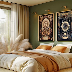 May include: Two framed illustrations of the sun and moon with intricate details and a dark background. The frames are hanging on a sage green wall above a bed with a white duvet and a brown throw blanket.