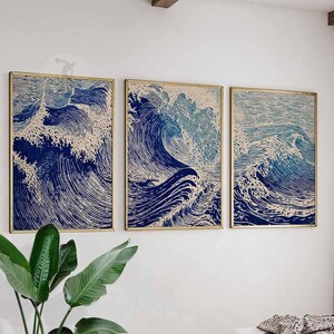 May include: Three framed art prints depicting stylized ocean waves in shades of blue and white. The artwork has a woodcut style, with detailed lines creating the wave patterns. The frames are gold-colored, and the prints are displayed on a white wall.