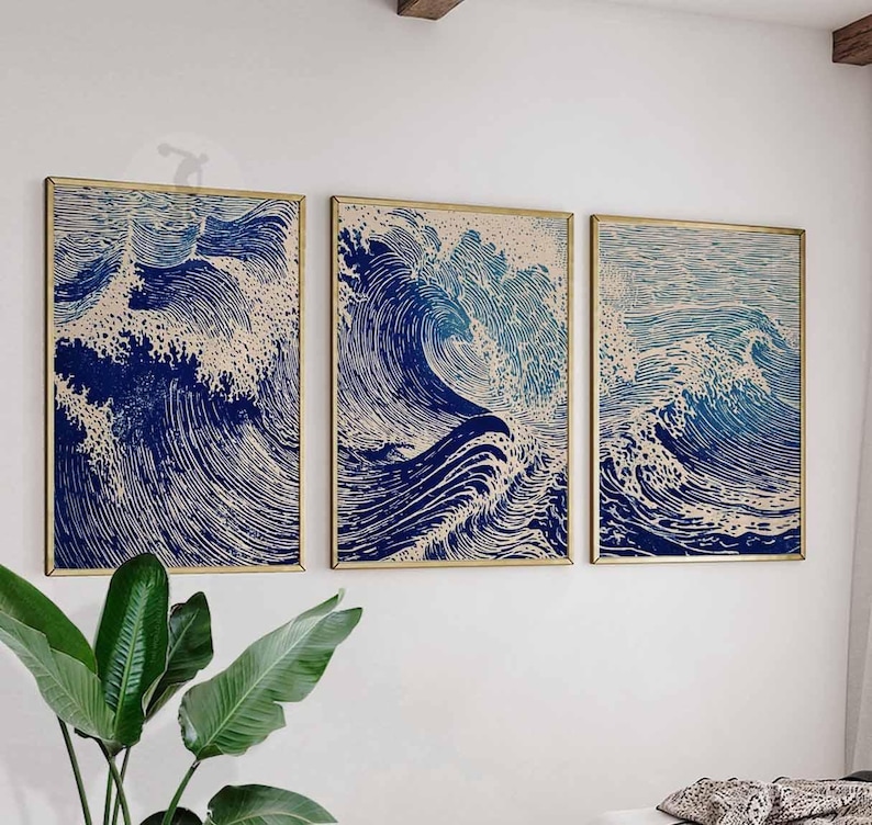 May include: Three framed art prints depicting stylized ocean waves in shades of blue and white. The artwork has a woodcut style, with detailed lines creating the wave patterns. The frames are gold-colored, and the prints are displayed on a white wall.