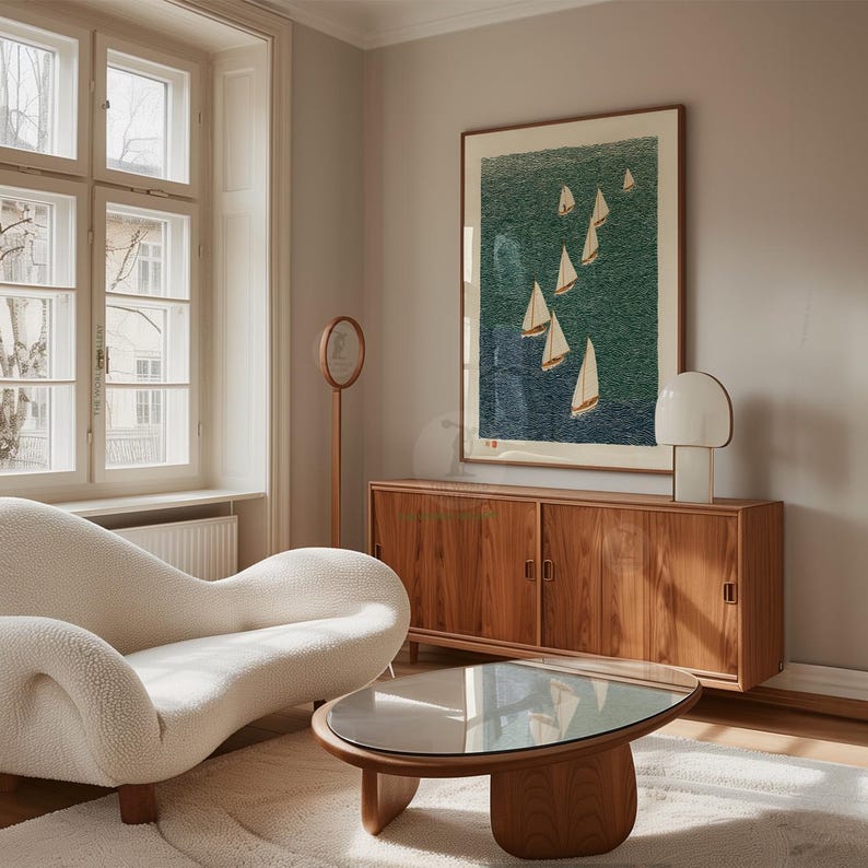 May include: A living room scene featuring a cream-colored, curved sofa, a wooden coffee table with a glass top, and a wooden cabinet. A framed artwork depicting sailboats on a teal sea hangs on the wall. A white lamp and a standing mirror are also visible.
