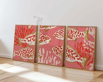May include: Three framed art prints featuring a repeating pattern of fish and coral. The fish are white with red spots and gold fins, set against a pink background. The coral is red and white. The frames are a light wood color.