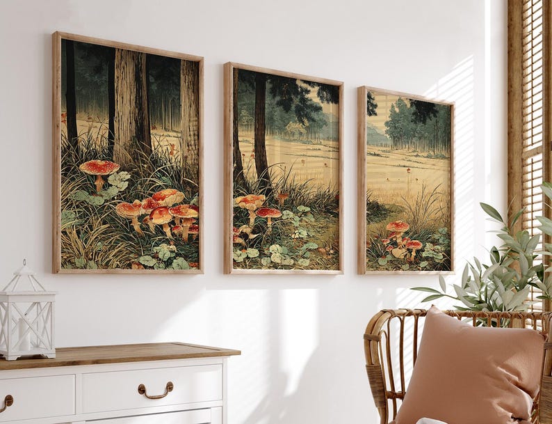 May include: Three framed art prints depicting a forest scene with red-capped mushrooms. The artwork has a vintage aesthetic, with tall trees and a grassy foreground. The frames are made of light-coloured wood, and the overall colour palette is muted.