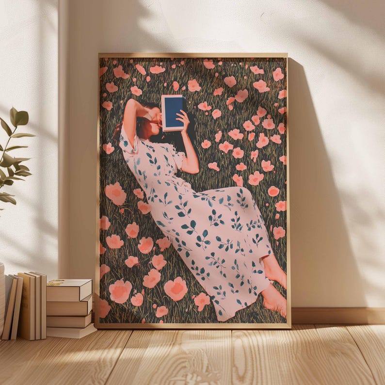K&ouml;nnte beinhalten: Ein gerahmter Kunstdruck zeigt eine Person, die in einem Feld mit rosa Blumen liegt und ein Buch liest. Die Person tr&auml;gt ein hellrosa Kleid mit blauen Bl&auml;ttermustern. Der Hintergrund ist ein dunkelgr&uuml;nes Feld mit verstreuten rosa Blumen. Der Rahmen ist hellbraun.