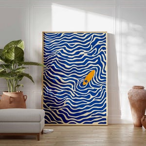May include: A framed art print featuring a blue and white wavy pattern with an orange surfboard in the center. The artwork is displayed in a room with a plant, ottoman, and decorative vases.