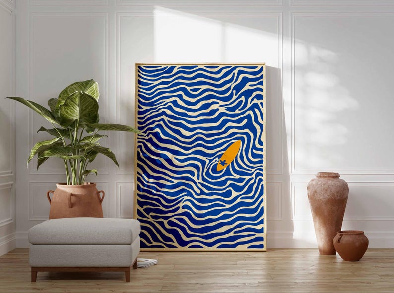 May include: A framed art print featuring a blue and white wavy pattern with an orange surfboard in the center. The artwork is displayed in a room with a plant, ottoman, and decorative vases.