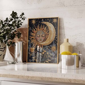 May include: A framed print of a celestial scene with a crescent moon and a sun with a face. The background is a dark blue with gold stars and a floral design.