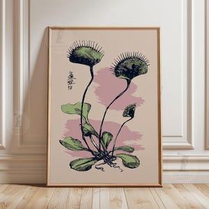 May include: Framed botanical print featuring a Venus flytrap illustration in green and black ink. The artwork includes Japanese characters and a pink and beige background. The print is displayed in a wooden frame.