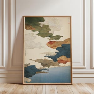 May include: A framed art print featuring a stylized depiction of clouds. The artwork showcases a palette of blues, greens, reds, and browns against a cream background. The print is displayed in a wooden frame and leans against a white wall.
