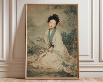 May include: Framed art print featuring a traditional Asian painting. The artwork depicts a woman in flowing white and blue robes, seated outdoors with a brush. The background shows a landscape with bamboo and a body of water. The frame is a warm, natural wood tone.
