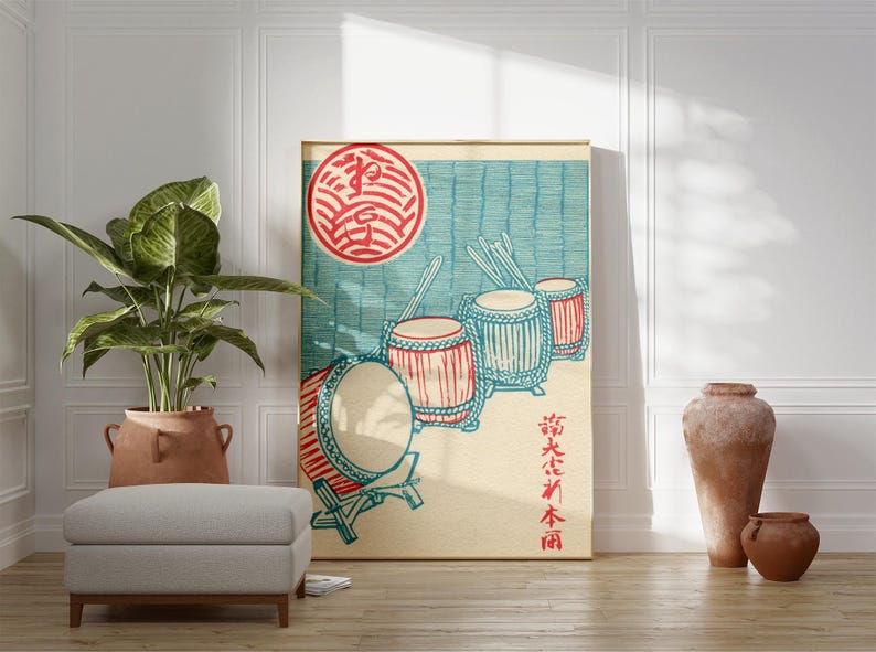 May include: A framed Japanese-style print featuring a red and blue illustration of drums and a red sun. The artwork is displayed in a room with a plant, a gray ottoman, and decorative pottery. The print has Japanese characters.