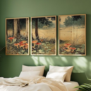 May include: Three framed art prints showing a forest scene with red-capped mushrooms. The artwork has a vintage aesthetic, with a palette of greens, browns, and beige. The frames are a light wood colour, and the prints are displayed on a green wall.