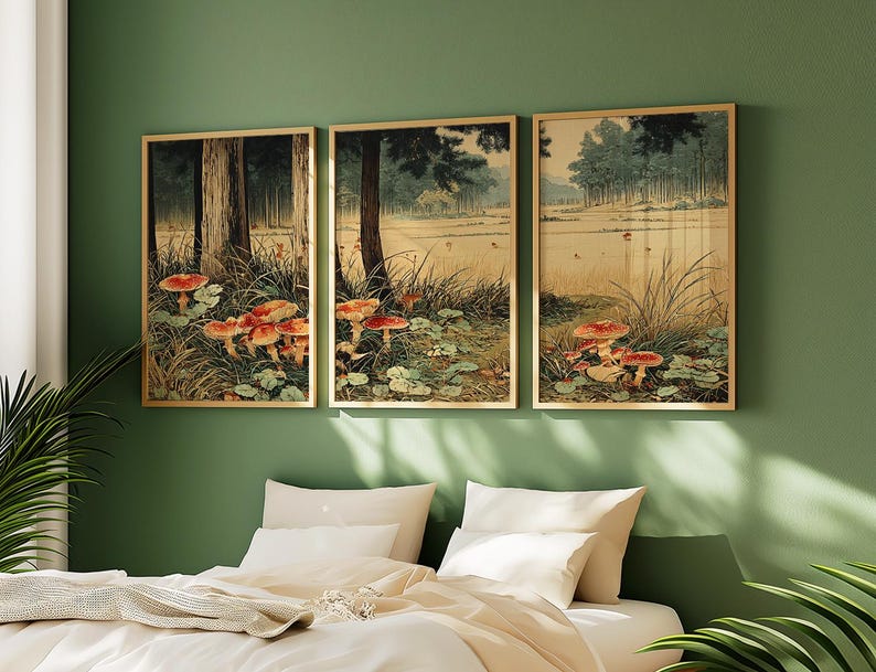 May include: Three framed art prints showing a forest scene with red-capped mushrooms. The artwork has a vintage aesthetic, with a palette of greens, browns, and beige. The frames are a light wood colour, and the prints are displayed on a green wall.