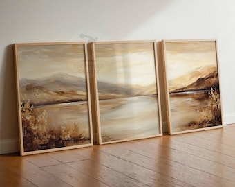 Puede incluir: Tres pinturas abstractas de paisajes enmarcadas en tonos apagados de marrón, beige y blanco. Las pinturas representan un lago con montañas en el fondo. Los marcos son de madera clara.