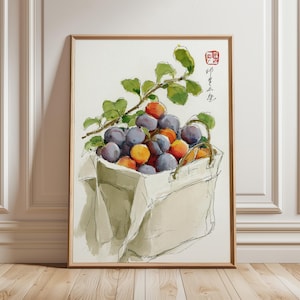 Op de afbeelding: Aquarel schilderij van een mand gevuld met pruimen en abrikozen, met groene bladeren en een tak die zich over de bovenkant uitstrekt. De mand is lichtbeige van kleur en het fruit is een mix van paars, oranje en geel. Het kunstwerk is ingelijst in een lichtbruine houten lijst.