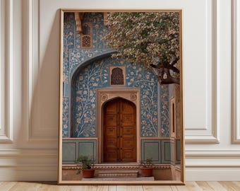 May include: Framed print of an ornate doorway with a wooden door, set against a teal wall adorned with floral patterns. A tree with white blossoms partially frames the entrance. Two potted plants sit at the base of the door.