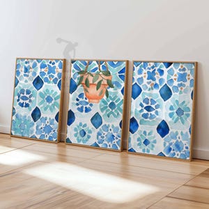 Może przedstawiać: Trzy oprawione wydruki akwarelowe. Wydruki przedstawiają niebieski i turkusowy wzór kwiatowy. Jeden wydruk ma wiszący doniczkę z terakoty z zielonymi liśćmi. Ramki są w kolorze jasnobrązowym.