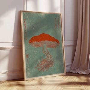 May include: A framed art print featuring a stylized orange mushroom illustration against a teal background. The artwork has a vintage aesthetic, with Japanese text and a wooden frame. The print is leaning against a white wall and wooden floor.