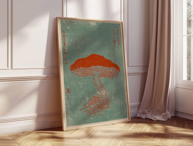 May include: A framed art print featuring a stylized orange mushroom illustration against a teal background. The artwork has a vintage aesthetic, with Japanese text and a wooden frame. The print is leaning against a white wall and wooden floor.
