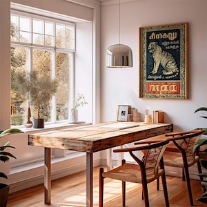 May include: A rustic wooden table with metal legs and two woven chairs. A framed poster with a tiger illustration hangs on the wall. A large window with a view of trees is in the background. A silver pendant light hangs above the table.