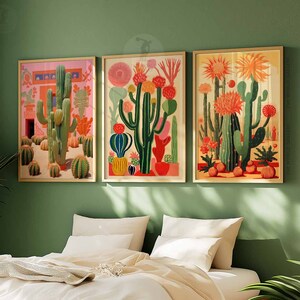 May include: Three framed illustrations of cacti in a variety of colors and styles. The cacti are set against a pink, green, and yellow background. The frames are a light wood color.