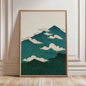 Op de afbeelding: Een ingelijste kunstdruk met een gestileerd landschap. Het kunstwerk toont turquoise bergen en witte wolken tegen een crèmekleurige lucht. De bergen en wolken hebben een textuur, en de lijst is lichtbruin.