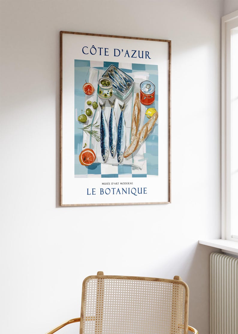 May include: A framed art print featuring a still life of French cuisine. The image includes sardines, olives, tomatoes, and bread on a blue and white checkered tablecloth. Text at the top reads "C&Ocirc;TE D'AZUR" and at the bottom "LE BOTANIQUE".
