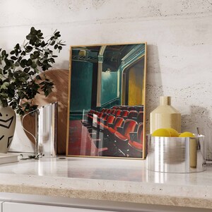 May include: A framed painting of a theater interior with red velvet seats. The painting is in a gold frame and is hanging on a white wall. There are two silver pitchers and a bowl of lemons in the foreground.