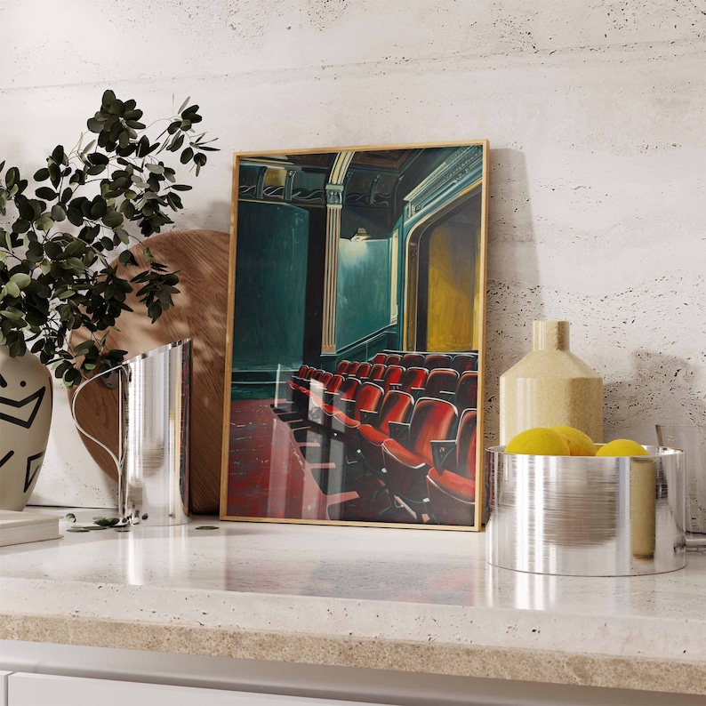 May include: A framed painting of a theater interior with red velvet seats. The painting is in a gold frame and is hanging on a white wall. There are two silver pitchers and a bowl of lemons in the foreground.