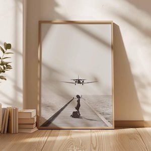 Puede incluir: Una impresi&oacute;n enmarcada en tonos sepia muestra a una mujer con equipaje en un muelle de madera, con un avi&oacute;n volando por encima. El muelle se extiende hacia el mar, con el cielo y el agua fusion&aacute;ndose en el fondo. La impresi&oacute;n est&aacute; en un marco de madera clara.