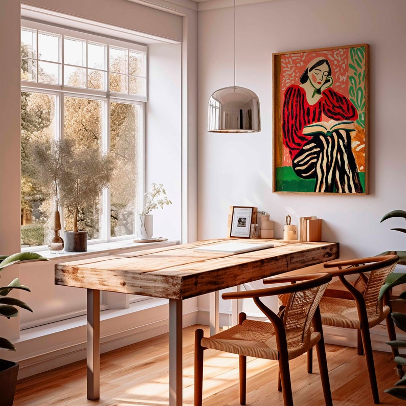 May include: A wooden table with a metal frame sits in a room with a large window and a painting of a woman in a red and white striped dress. The painting is framed in wood and hangs on a white wall. Two chairs with woven seats are placed at the table.