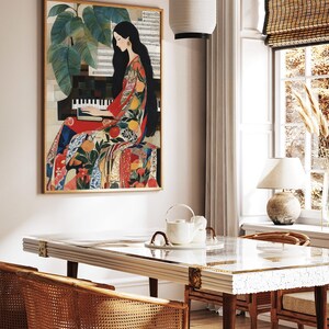May include: A framed artwork shows a woman playing a piano, dressed in a vibrant patterned gown. The artwork is in a room with a white table, rattan chairs, and a window with a bamboo blind. A white paper lantern hangs from the ceiling.