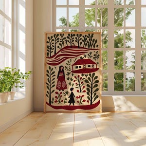 Op de afbeelding: Een ingelijste folk art print met een rood en zwart landschap met gestileerde figuren, bomen en een huis. Het kunstwerk wordt tentoongesteld in een lichte kamer met een raam en potplanten, wat een warme en uitnodigende sfeer cre&euml;ert.
