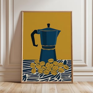 May include: A framed art print depicting a blue coffee maker and coffee beans on a mustard yellow backdrop. The coffee maker is positioned above a cluster of coffee beans on a blue and white patterned surface. The artwork is in a wooden frame.