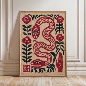 May include: Framed art print depicting a red snake with detailed patterns, set against a beige backdrop with red roses and black foliage. A red hand and a square with text are also included. The artwork is in a wooden frame.