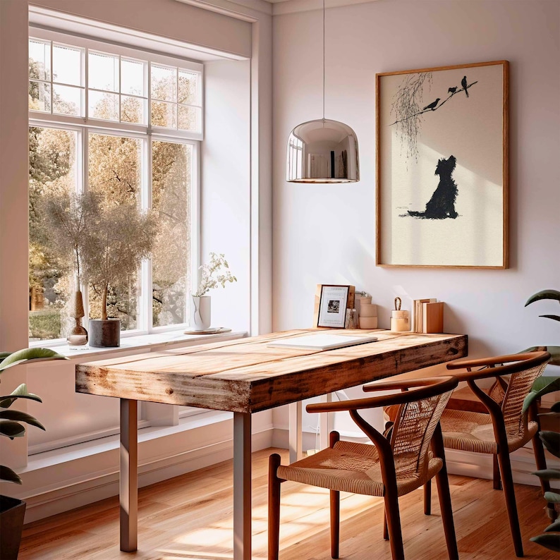 K&ouml;nnte beinhalten: Ein heller, luftiger Raum mit einem Holztisch und zwei St&uuml;hlen. An der Wand h&auml;ngt ein gerahmtes Kunstwerk eines Hundes, der V&ouml;gel betrachtet. Ein gro&szlig;es Fenster bietet einen Blick auf B&auml;ume. &Uuml;ber dem Schreibtisch h&auml;ngt eine silberne Pendelleuchte.