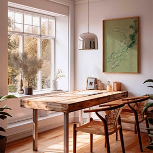 May include: A sunlit home office featuring a large wooden desk with metal legs, two woven chairs, and a framed artwork depicting fish. A large window offers a view of trees. A chrome pendant light hangs above the desk, and plants add a touch of nature.