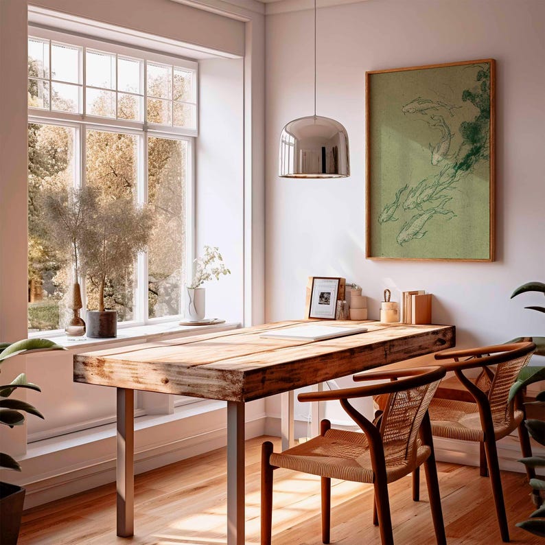 May include: A sunlit home office featuring a large wooden desk with metal legs, two woven chairs, and a framed artwork depicting fish. A large window offers a view of trees. A chrome pendant light hangs above the desk, and plants add a touch of nature.