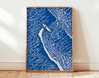 May include: A framed art print featuring a surfer on a yellow surfboard in the ocean. The artwork has a blue and white color scheme, with the ocean waves depicted in detail. The print is displayed in a wooden frame.
