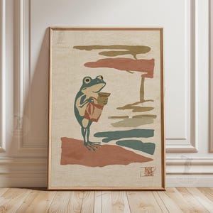 May include: Framed art print featuring a stylized frog holding a pot and a bag. The frog is depicted in shades of green and blue, standing on a reddish-brown surface. The background includes horizontal bands of color in muted tones of brown, green, and red.