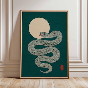 May include: Framed art print depicting a stylized snake with a red tongue and eyes, coiled before a full moon. The artwork uses green and beige tones, with a Japanese aesthetic. The print is presented in a wooden frame.