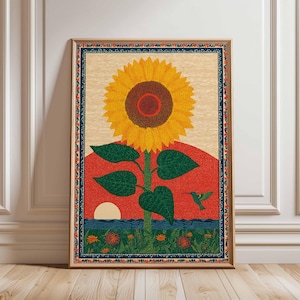 Op de afbeelding: Een ingelijste kunstdruk met een grote zonnebloem met gele bloemblaadjes en een bruin hart. Het kunstwerk bevat een rode zonsondergang, blauw water en een groene kolibrie. De print heeft een decoratieve rand en een lichte houten achtergrond.