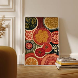 May include: A framed art print featuring a colorful still life of food. The artwork includes plates of pasta, tomatoes, oranges, and other decorative elements in shades of red, green, and yellow. The print is leaning against a white wall.