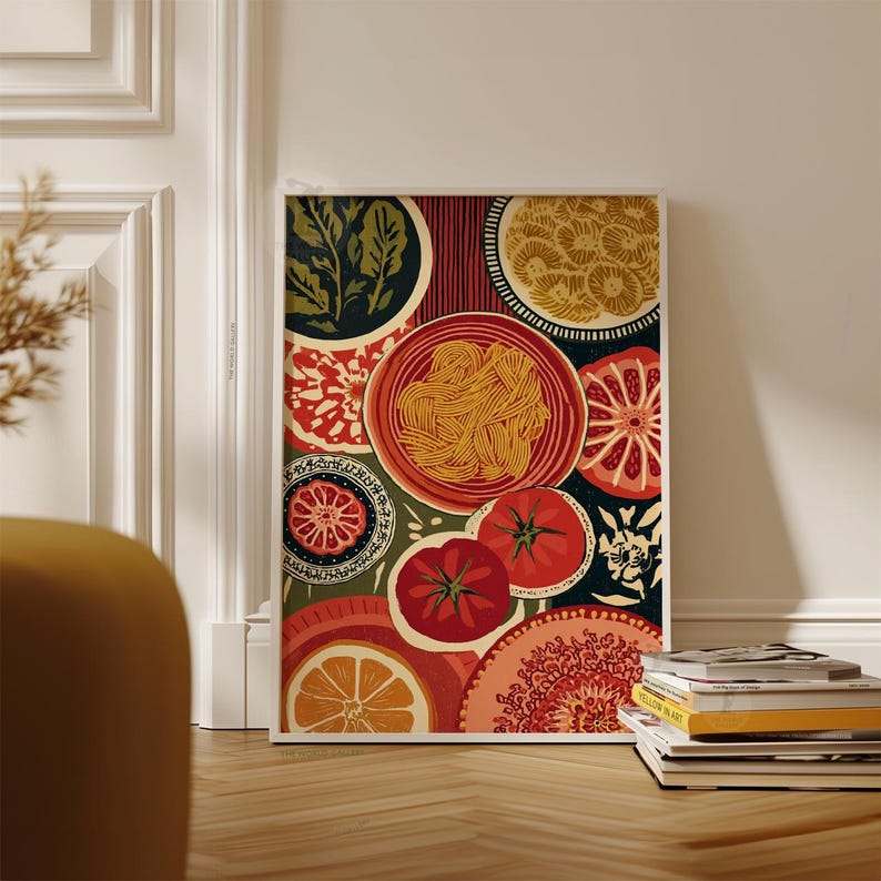 May include: A framed art print featuring a colorful still life of food. The artwork includes plates of pasta, tomatoes, oranges, and other decorative elements in shades of red, green, and yellow. The print is leaning against a white wall.