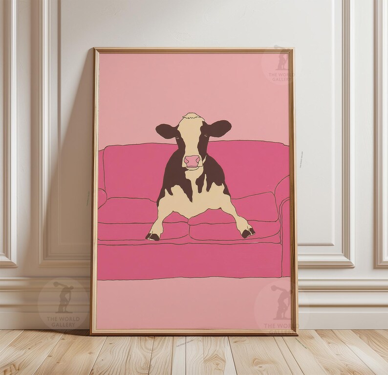 May include: Framed art print showing a cow relaxing on a pink sofa. The cow is illustrated in black and white, set against a pink backdrop and sofa. The artwork has a minimalist, modern style, ideal for home decor.
