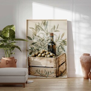 May include: A framed watercolor print featuring a wooden crate filled with olives, a dark glass bottle, and olive branches. The artwork is displayed in a room with a potted plant, a footstool, and terracotta vases.